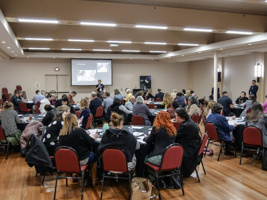 A large room filled with round table and people engaging in discussion.