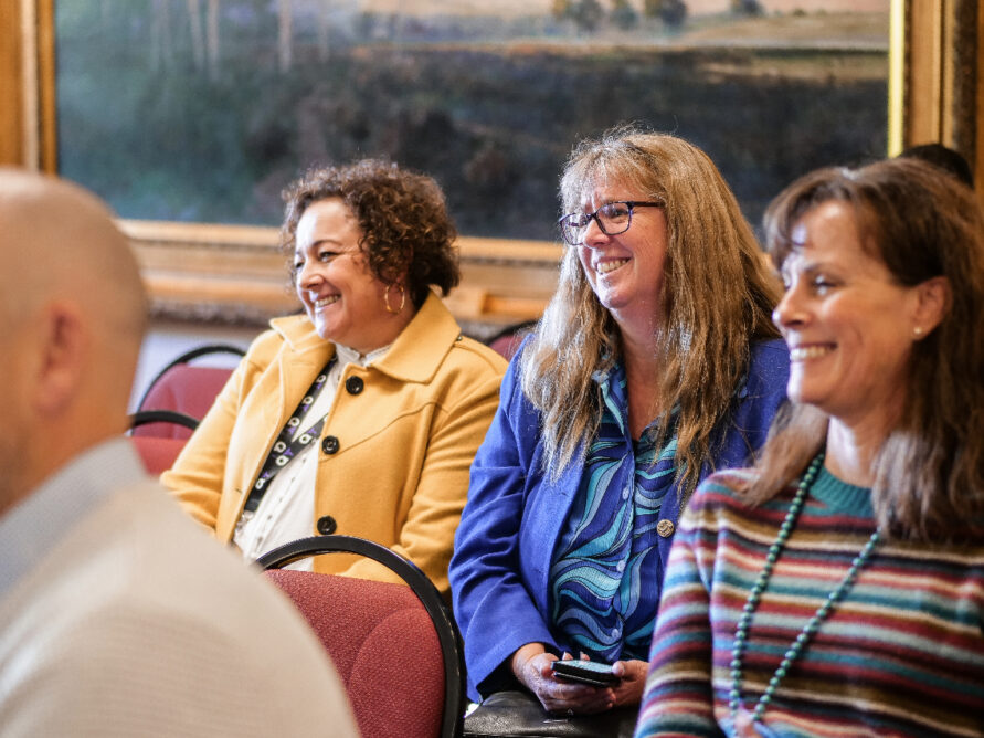 Two women smiling watching a QTiP23 presentation.