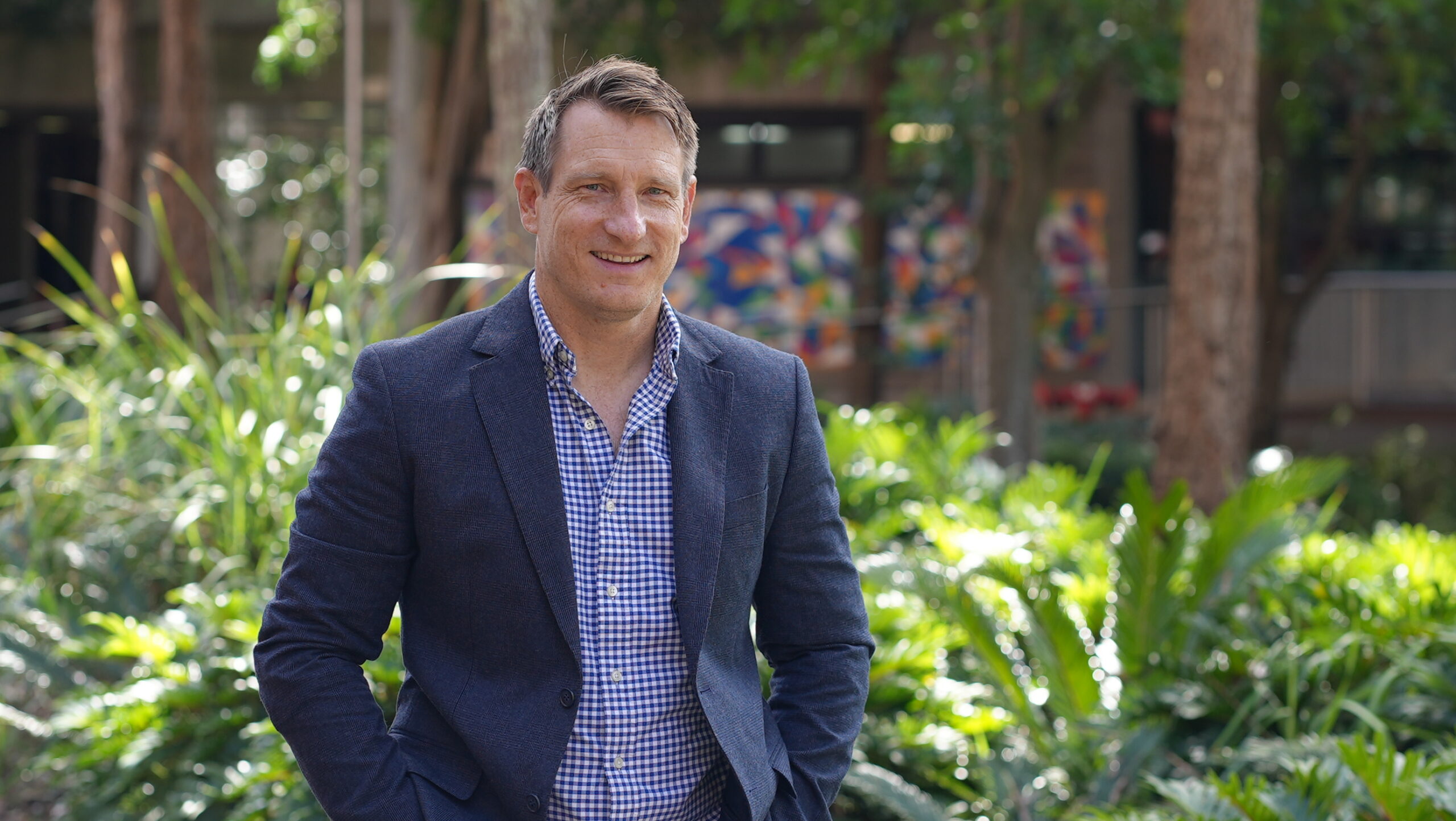 Dr Drew Miller in blue blazer standing in front of greenery.